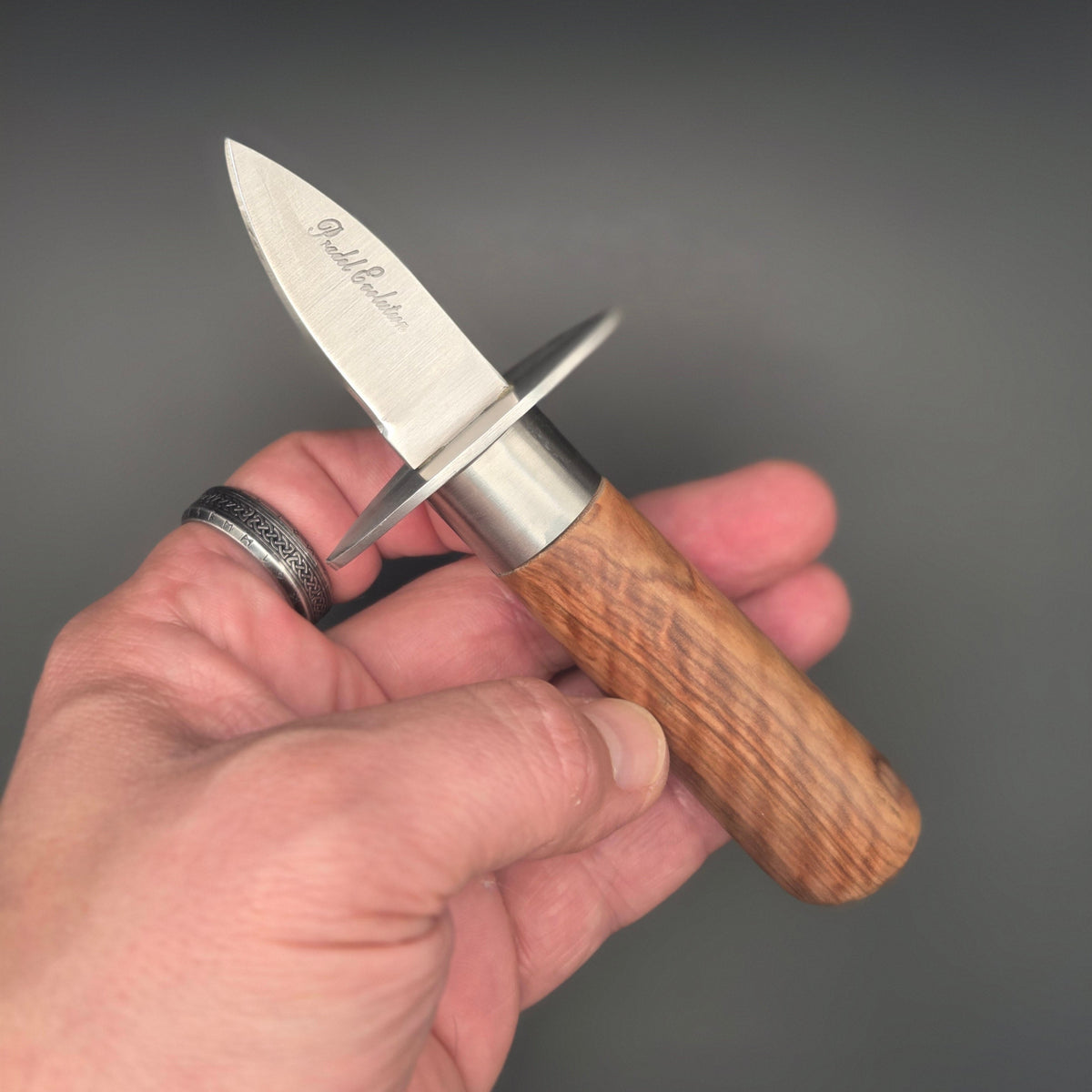 Couteau à huître tenu dans une main. On y voit son manche en teck et il est muni d'une garde
