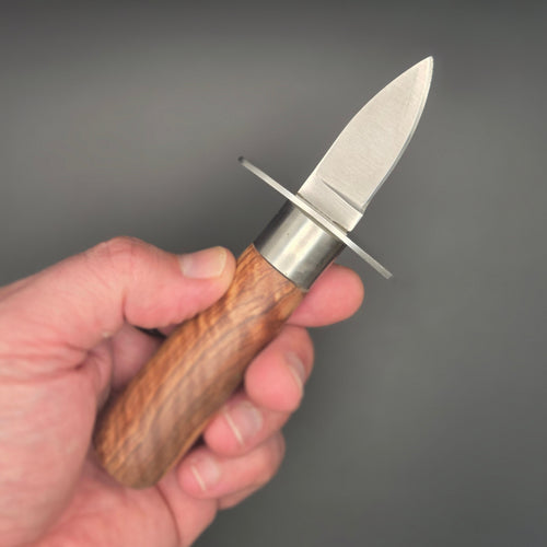 Couteau huître tenu dans une main. Il possède un manche en teck avec une garde.