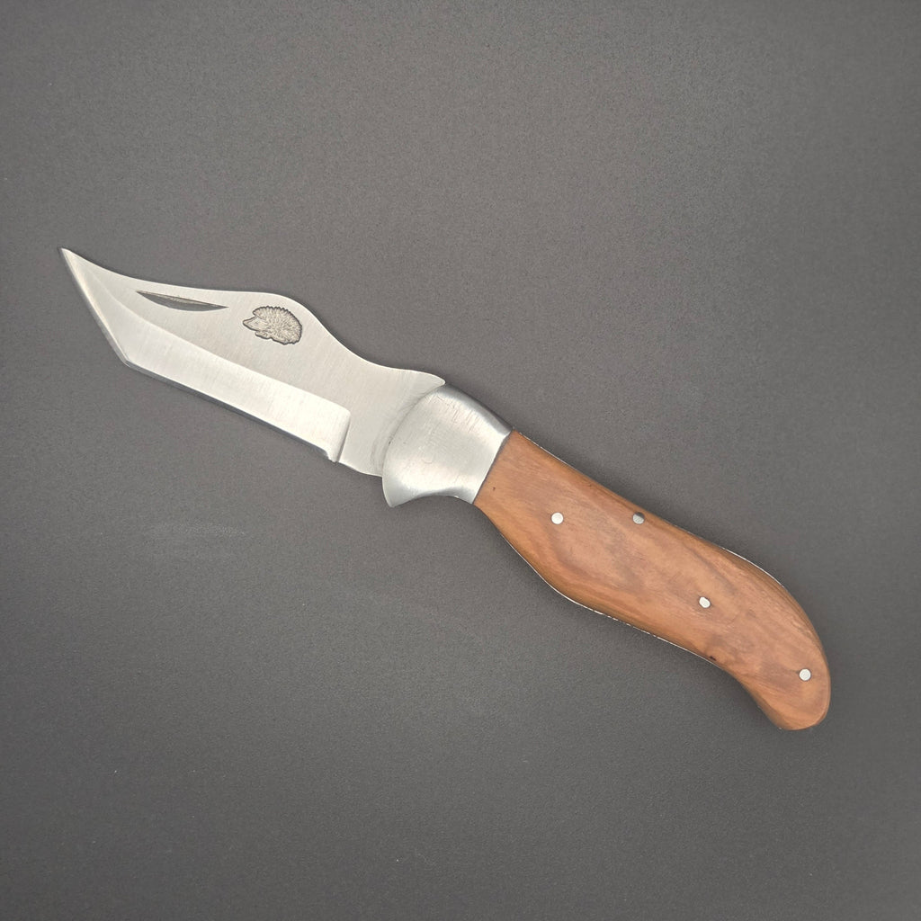 couteau robuste et pliant avec un manche en teck. Il est posé à plat et est ouvert. On voit la lame avec un hérisson gravé dessus. La qualité est du second choix