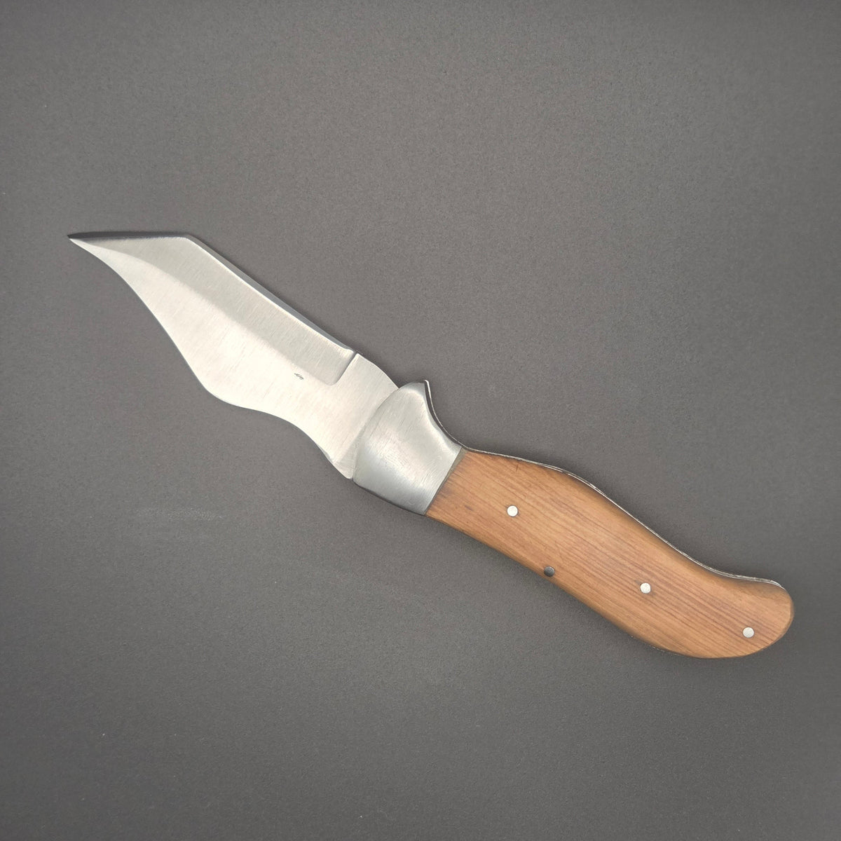 couteau utilitaire pliant posé à plat en position ouvert. Lame robuste à forme ondulée muni d'un manche en teck. La qualité est du second choix.