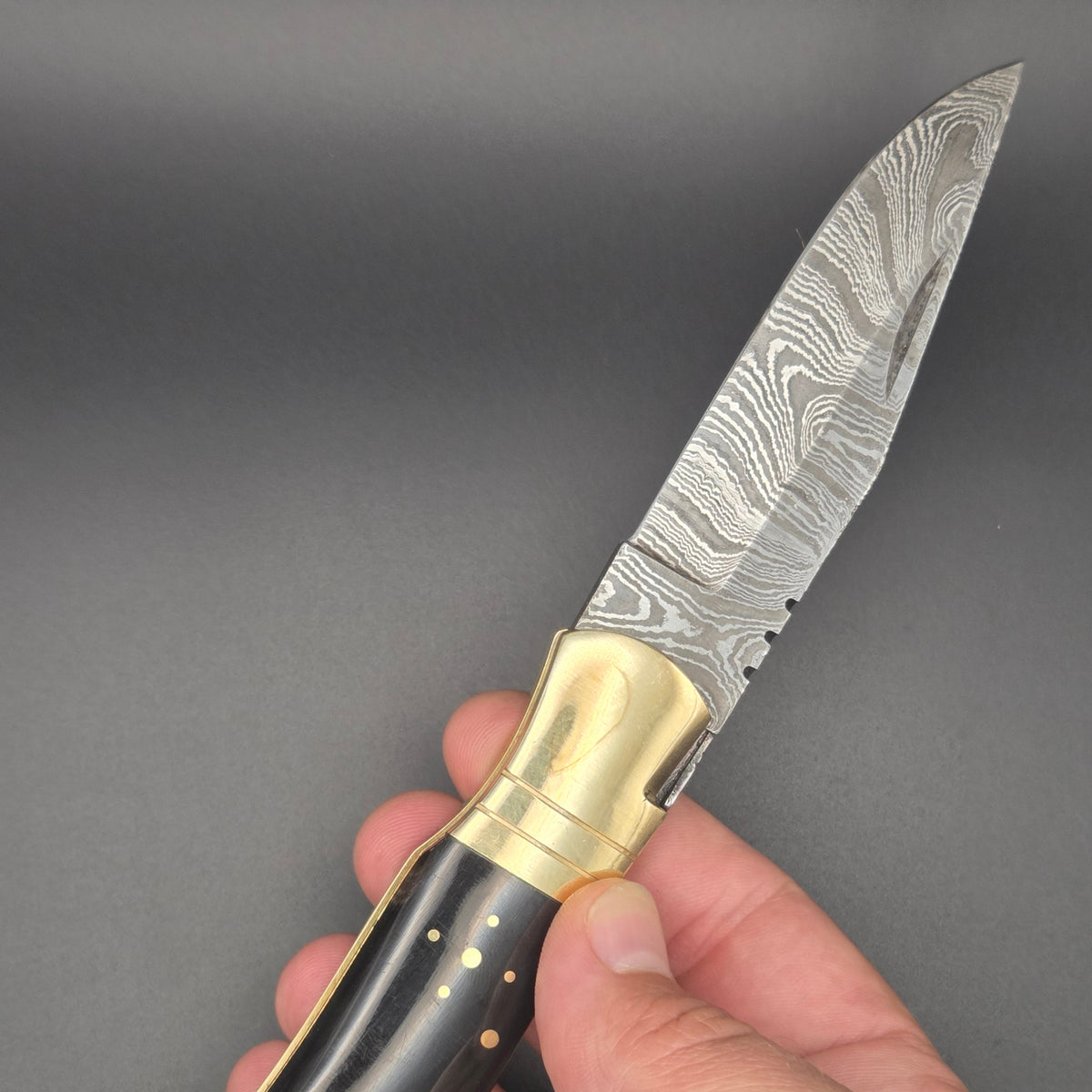 couteau lame damas ouvert et tenu dans une main