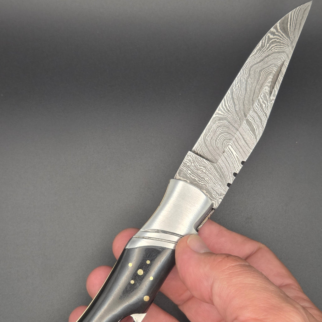 couteau utilitaire avec tire bouchon et lame damas ainsi qu'un manche en corne. Il est en position ouverte et tenu dans une main