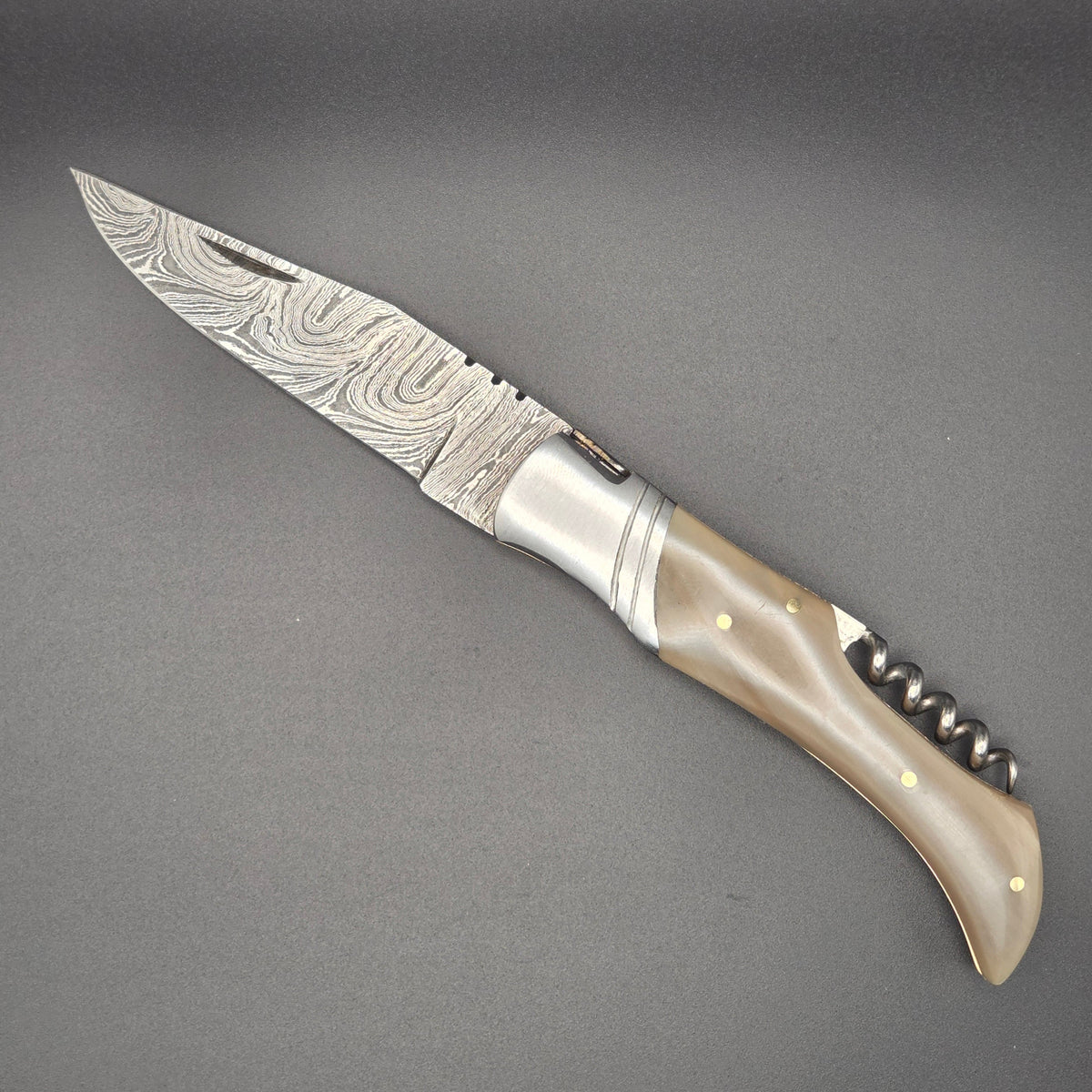 couteau utilitaire pliant avec une lame damas et tire-bouchon en position ouverte. Le manche est en corne blonde.