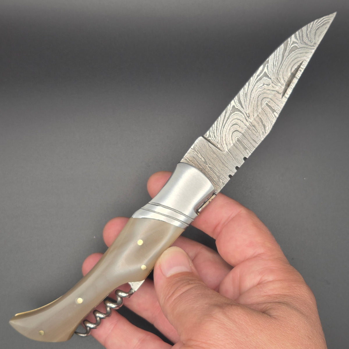 couteau pliant utilitaire avec lame damas et tire-bouchon tenu dans une main en position ouverte
