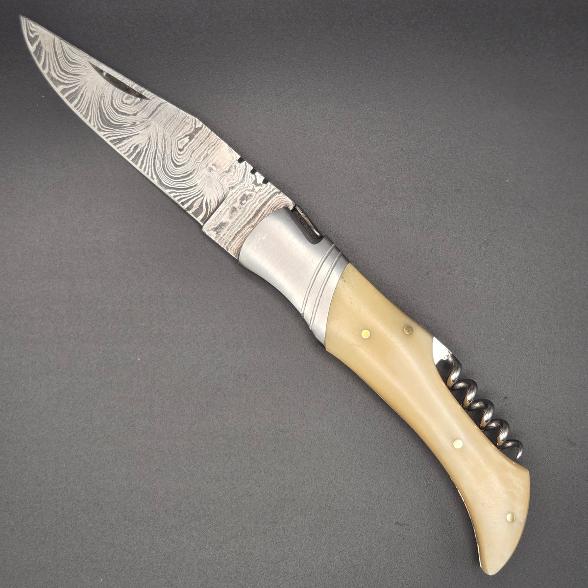 couteau utilitaire pliant en position ouverte muni d'une lame en damas et d'un tire-bouchon comme accessoire