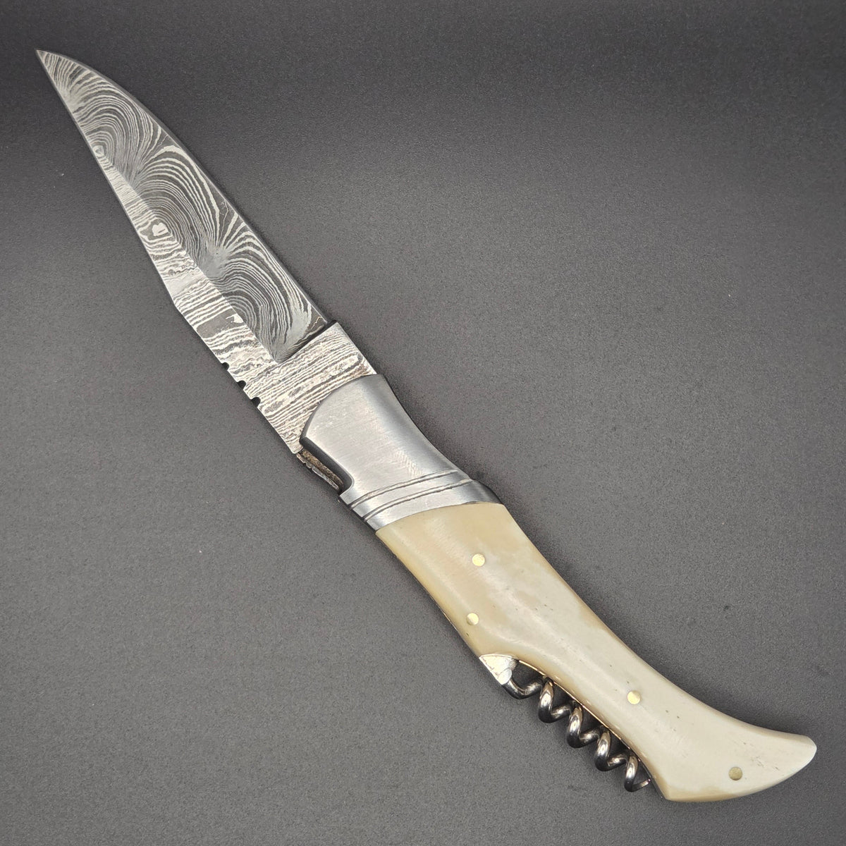 couteau utilitaire pliant avec lame en damas en position ouvert. on y voit aussi son manche en os et un tire-bouchon bien pratique