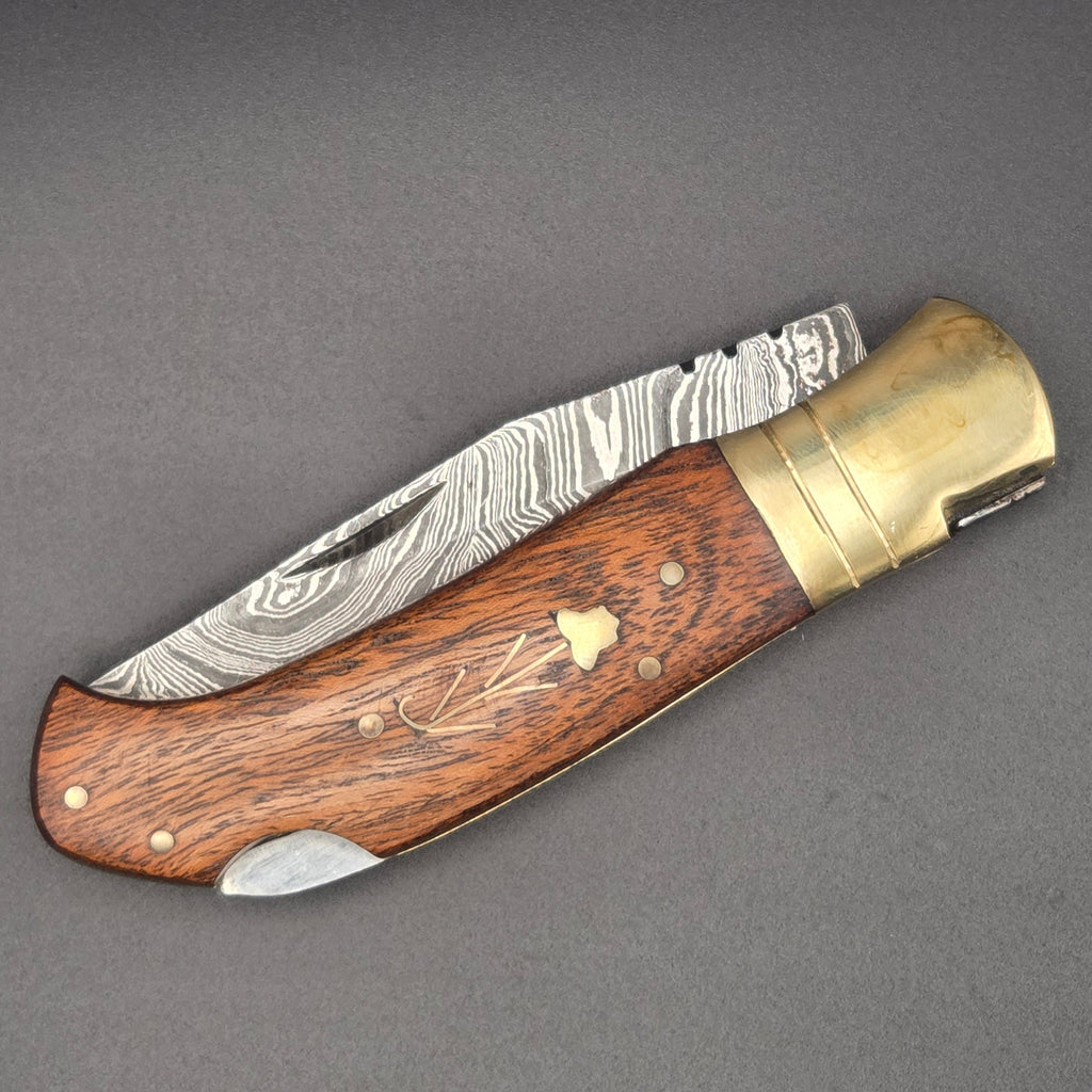 couteau pliant utilitaire en position fermée. On y voit une lame damas et un manche en noyer incrusté d'une fleur