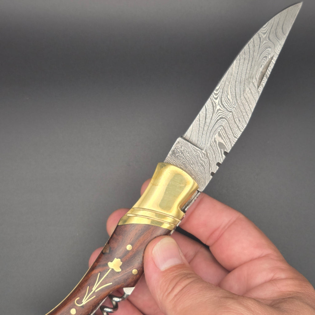 couteau utilitaire avec lame en damas et manche en noyer tenu en position ouverte dans une main.