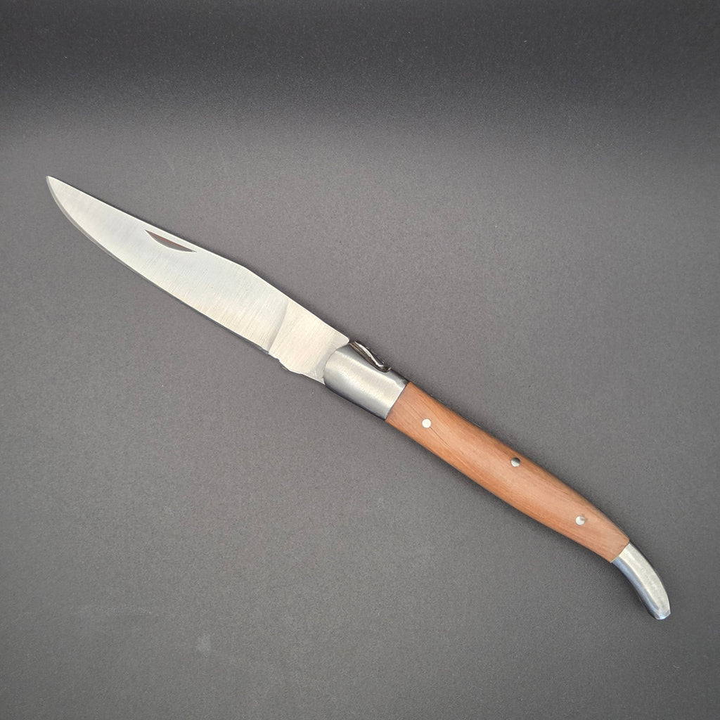 couteau pliant utilitaire élancé posé à plat en position ouvert. Il a un manche en bois de teck. La qualité globale du couteau est de second choix.