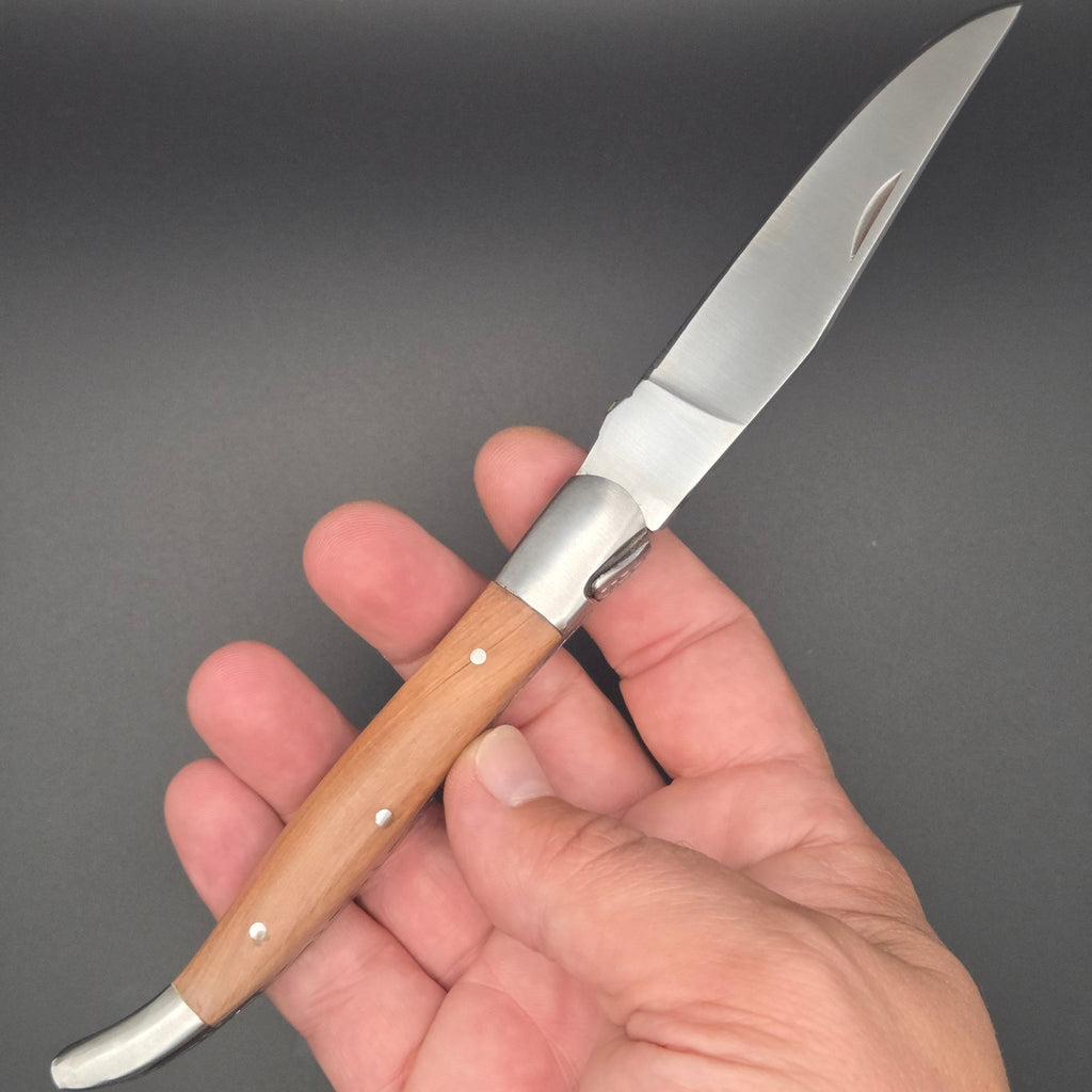 couteau utilitaire pliant élancé muni d'un manche en teck. Il est tenu dans une main et est en position ouvert. La qualité est de second choix.