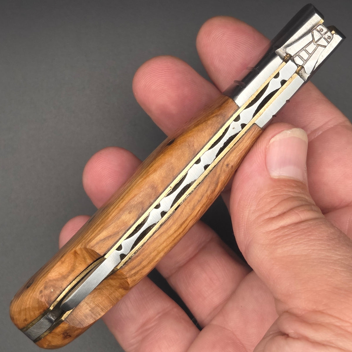 Vue du guillochage d'un couteau pliant utilitaire. Ce couteau possède une lame en damas et un manche en teck