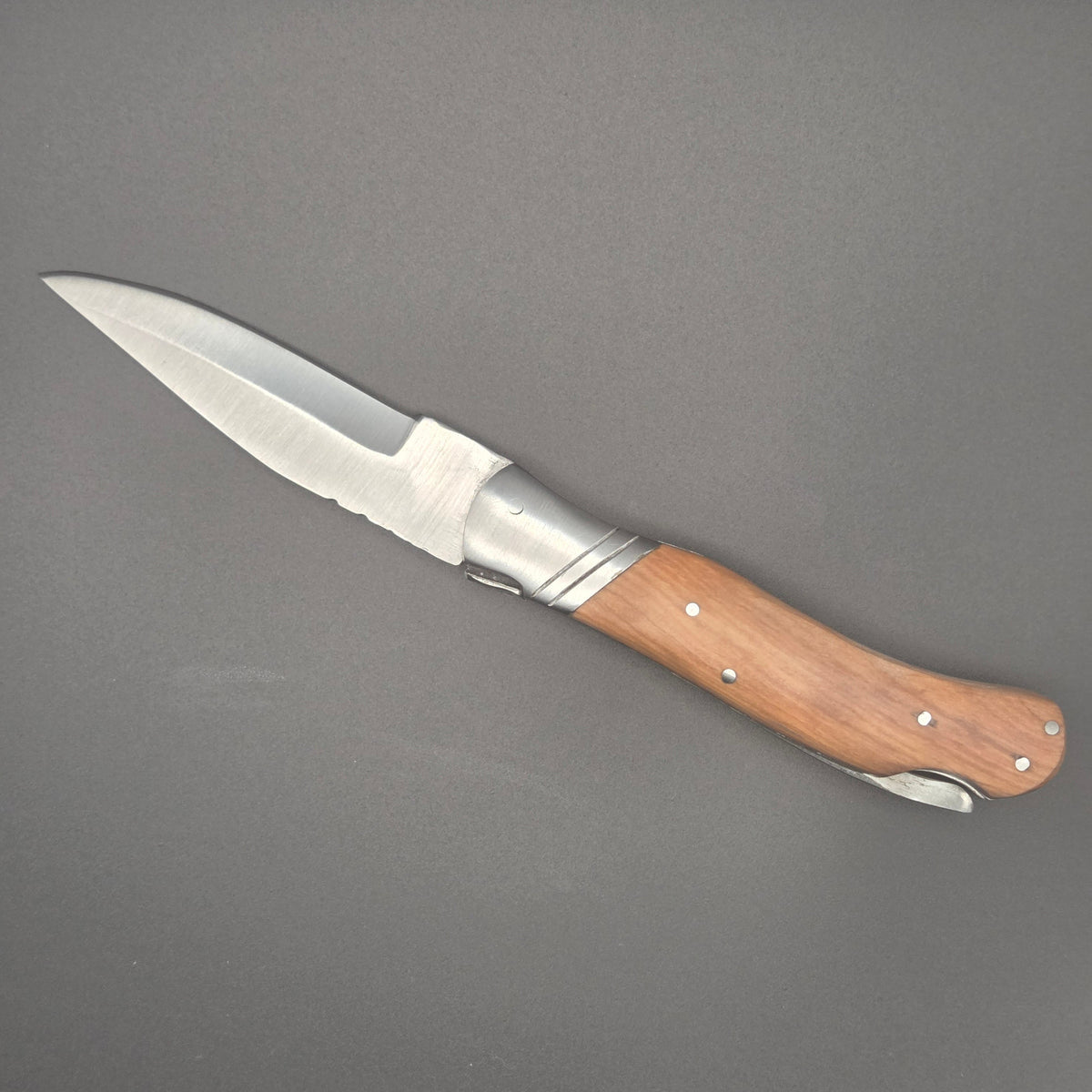 couteau pliant utilitaire posé à plat en position ouverte. Il possède un manche en teck.