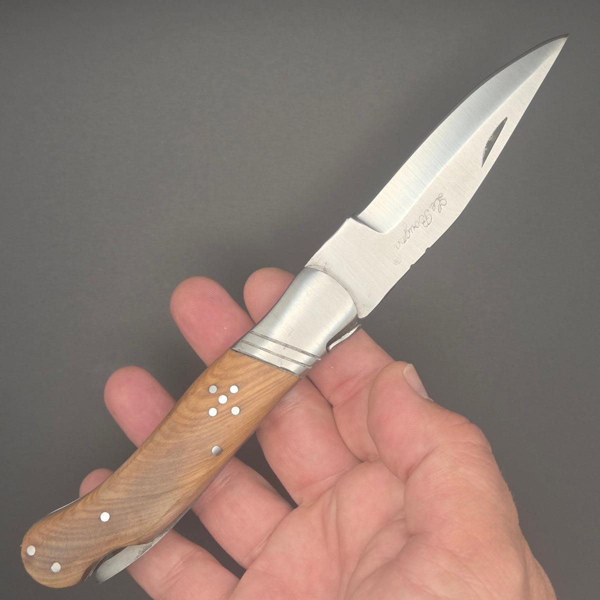 couteau pliant utilitaire tenu dans une main en position ouverte. Il a un manche en teck. c'est un couteau de second choix