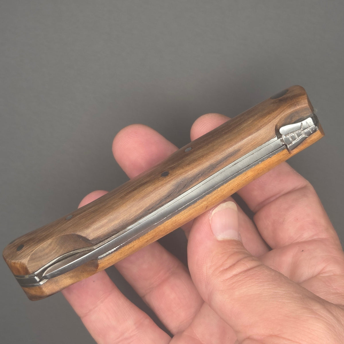Couteau pliant utilitaire tenu dans une main en position ouvert. On y voit son joli manche en bois.