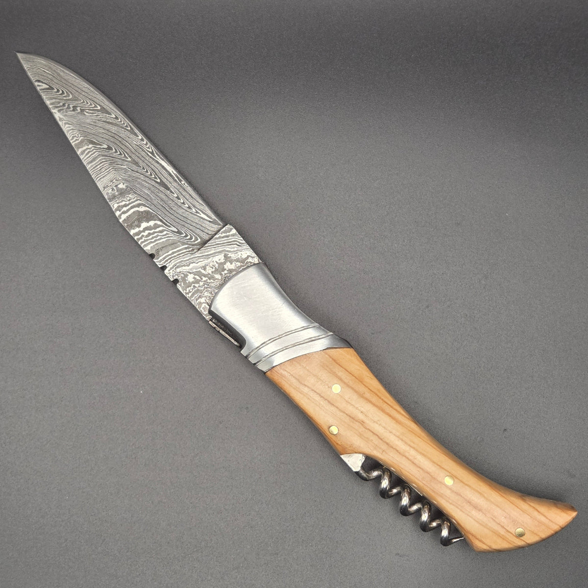 couteau pliant utilitaire avec lame en damas et tire-bouchon. Son manche est en teck. Il se trouve en position ouverte.