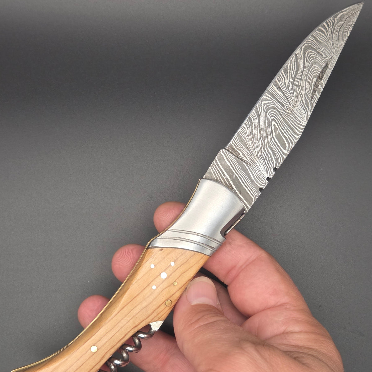 couteau lame damas utilitaire en position ouvert et tenu dans une main par son manche en teck