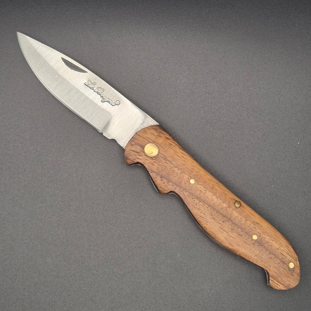 Couteau utilitaire pliant posé à plat en position ouvert avec son manche en marronnier.