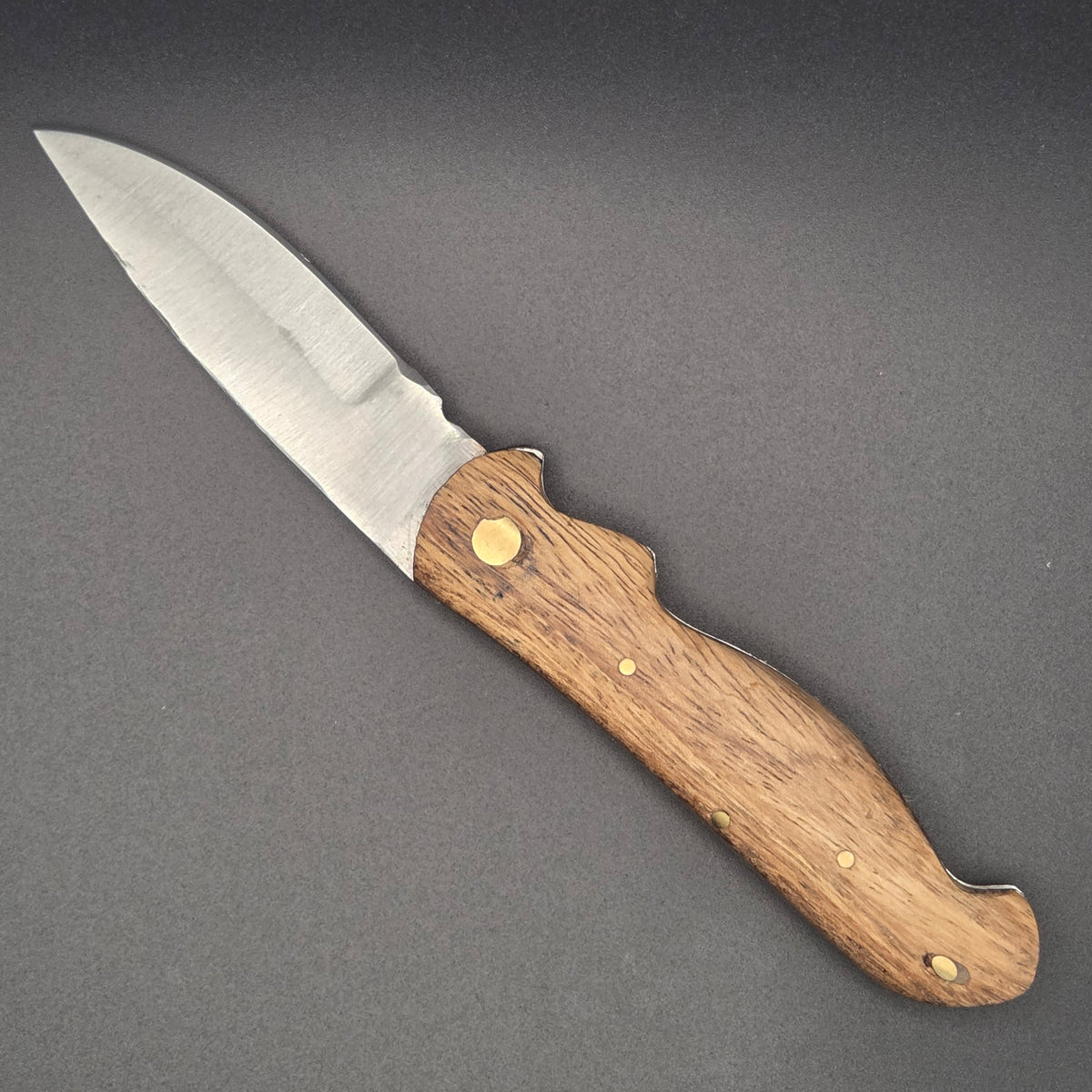 Couteau pliant utilitaire avec manche en marronnier posé à plat en position ouvert.