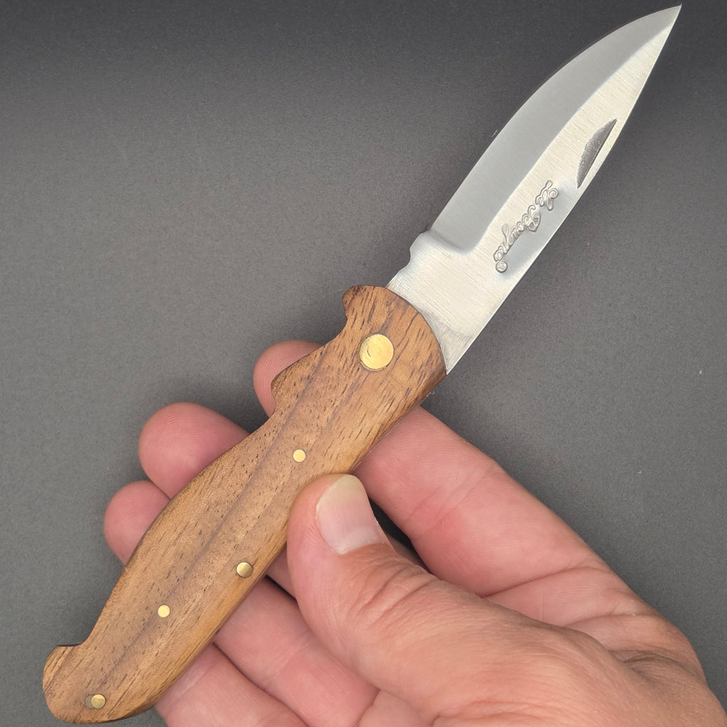Couteau pliant utilitaire tenu dans une main en position ouvert. Il possède un manche en marronnier. 