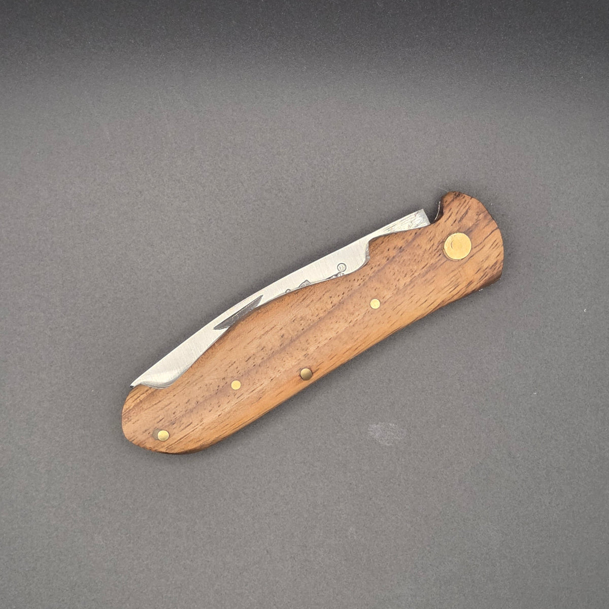 Couteau utilitaire pliant avec un manche en marronnier posé à plat en position fermé.