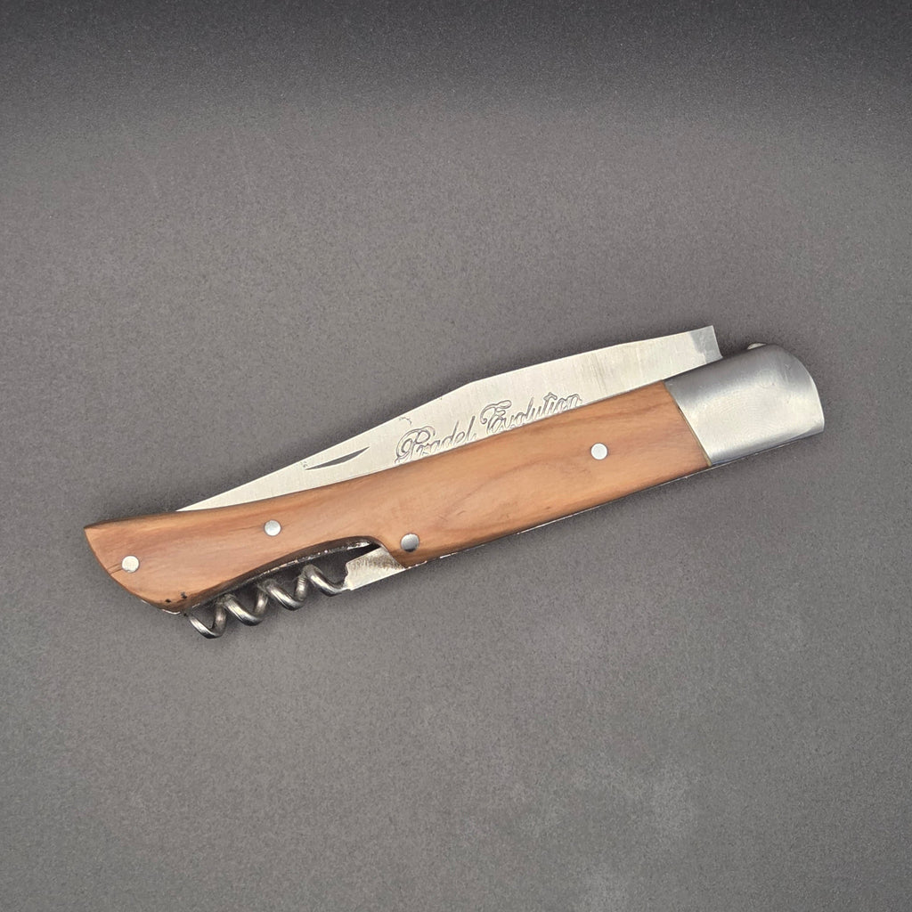 Couteau utilitaire pliant avec un manche en teck posé en position fermé. On y voit son tire-bouchon intégré au manche.