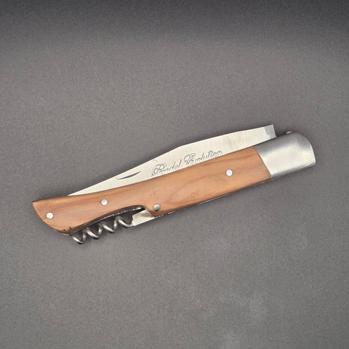 Couteau utilitaire pliant avec un manche en teck posé en position fermé. On y voit son tire-bouchon intégré au manche.