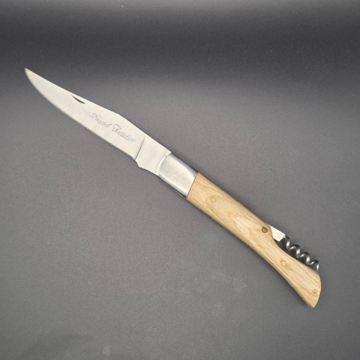 Couteau utilitaire pliant avec un manche en teck blanchi posé à plat en position ouvert. Il est muni d'un tire-bouchon
