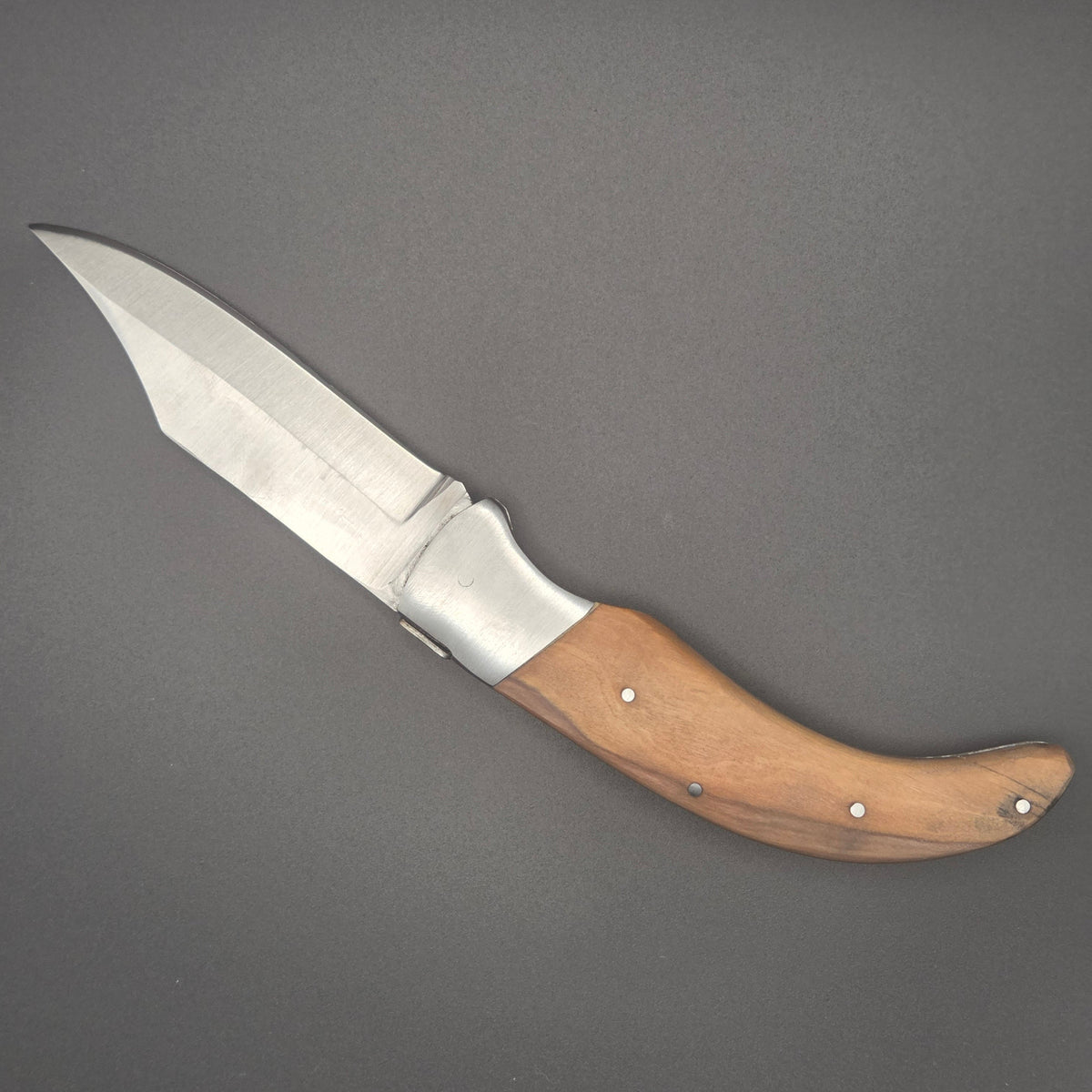 Couteau utilitaire pliant avec manche en teck incurvé posé à plat en position ouvert.