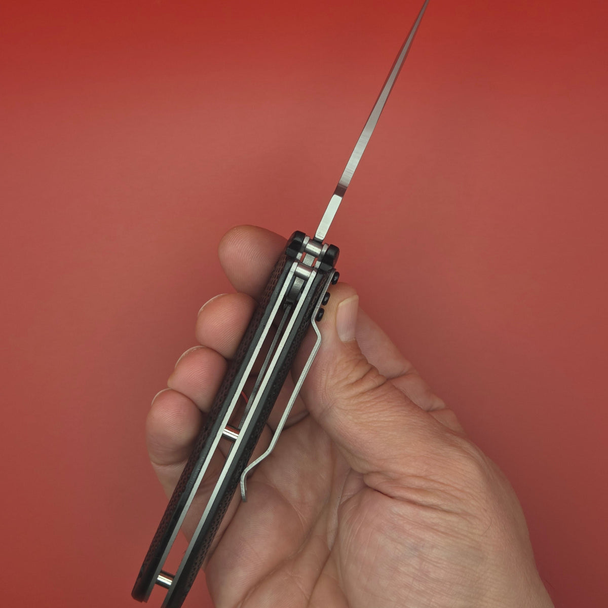 couteau pliant à manche noir tenu dans une main vue du dessus