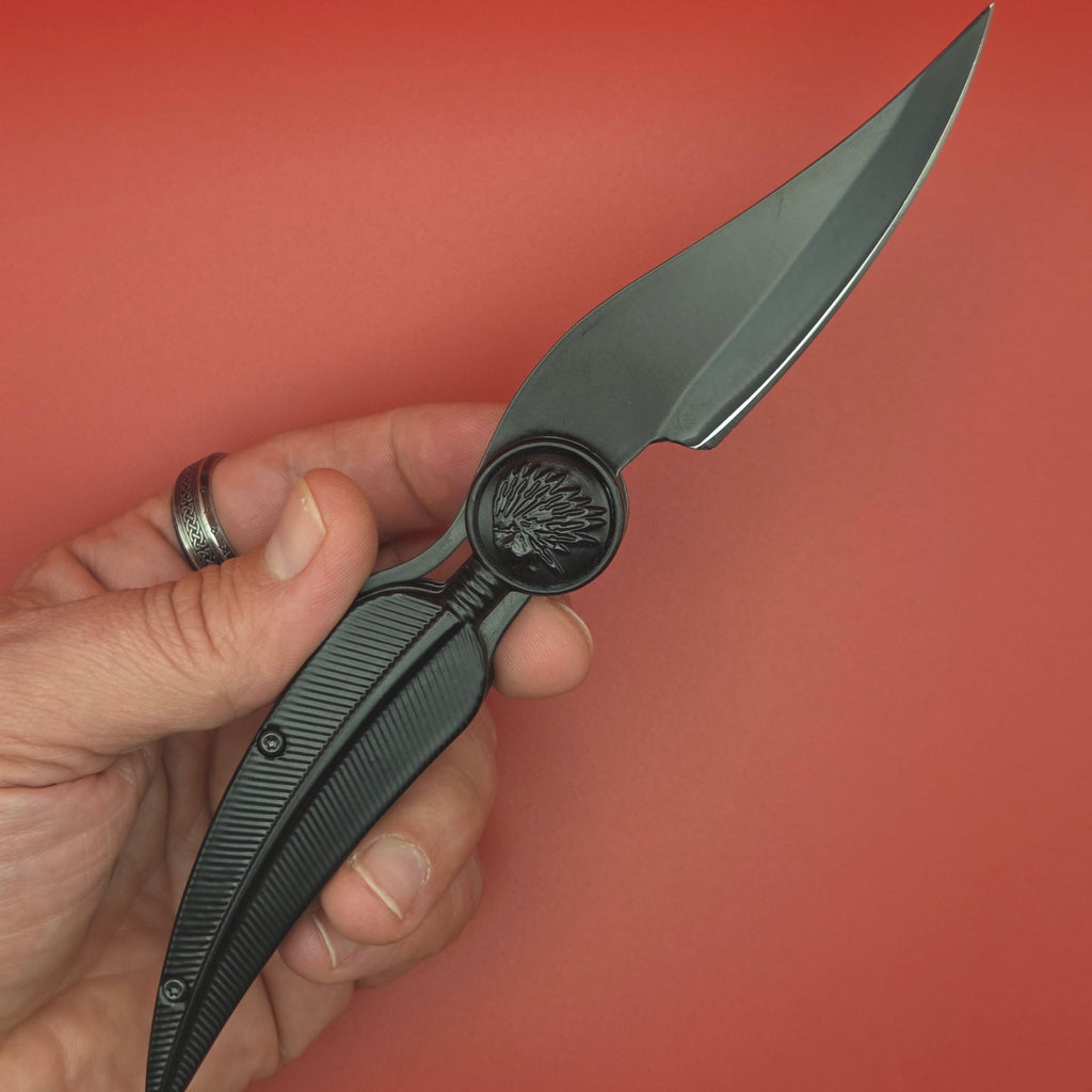 couteau pliant ouvert tenu dans une main. Il est en forme de plume noir et fait 10 cm.