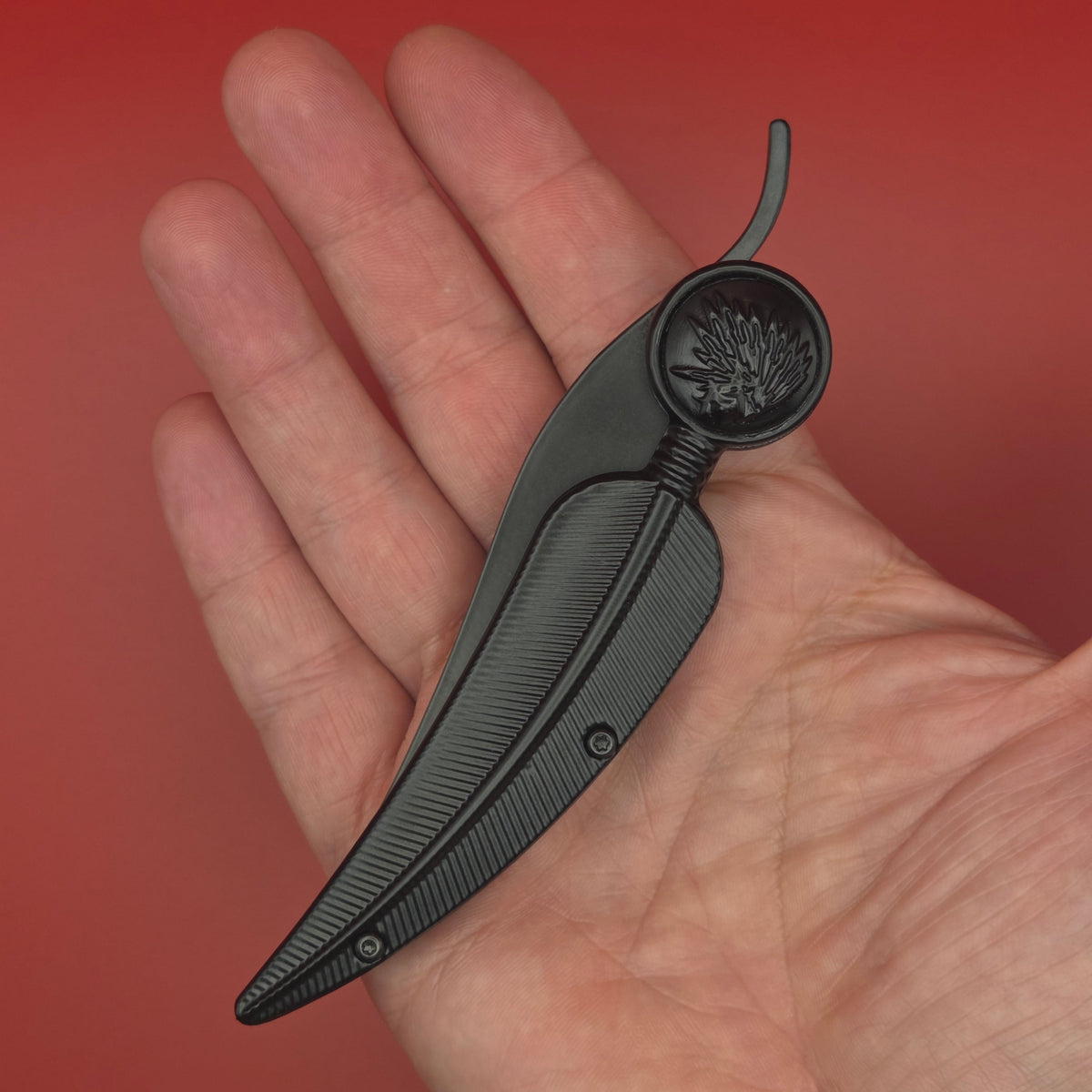 couteau noir en forme de plume. Il est fermé et se trouve dans la paume d'une main